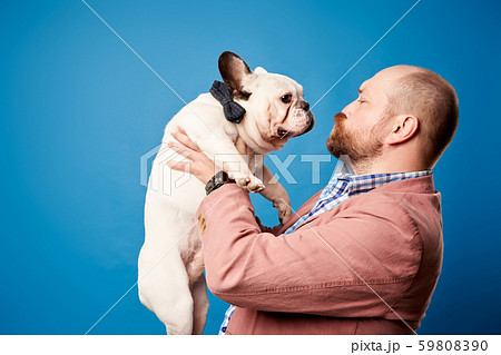 Bald man in jacket with french bulldog in his arms on empty blue background 59808390
