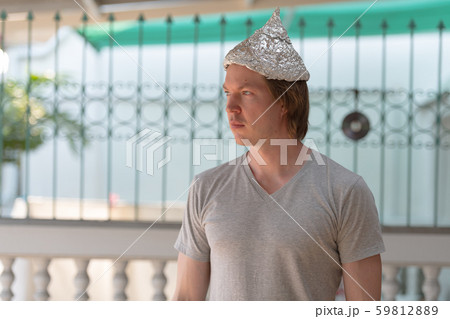 Young man with tin foil hat thinking as conspiracy theory concept outdoors 59812889