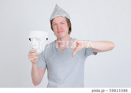 Young man with tinfoil hat holding white mask and giving thumbs down Young man with tinfoil hat holding white mask and giving thumbs down 59813386