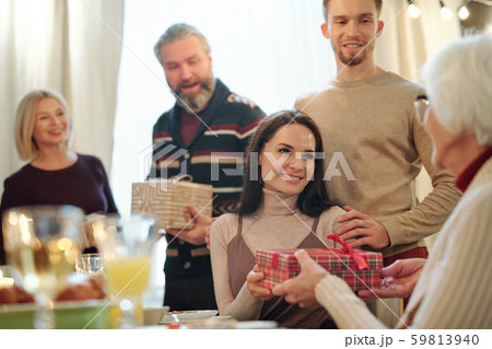 Young couple giving wrapped giftbox with Christmas present to granny 59813940