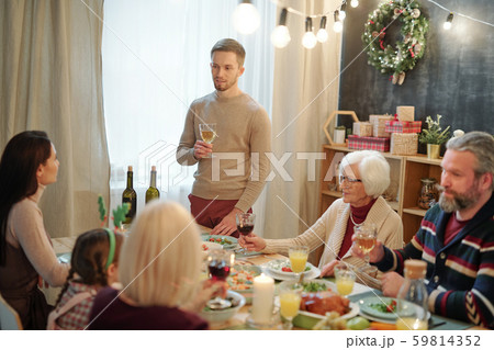 Young man with glass of wine making toast by served table in front of his family Young man with glass of wine making toast by served table in front of his family 59814352