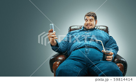 Fat man sitting in a brown armchair, emotional watching TV Fat man sitting in a brown armchair, emotional watching TV 59814414