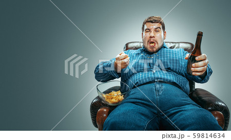 Fat man sitting in a brown armchair, emotional watching TV Fat man sitting in a brown armchair, emotional watching TV 59814634