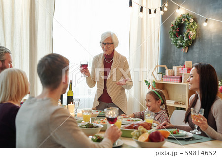 Senior grey-haired female toasting with glass of red wine in front of her family Senior grey-haired female toasting with glass of red wine in front of her family 59814652