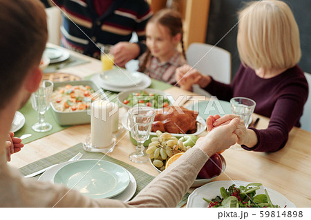 Hands of family held by each other over served festive table during pray Hands of family held by each other over served festive table during pray 59814898