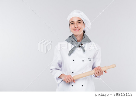Pretty young smiling chef in white uniform holding rolling-pin while cooking Pretty young smiling chef in white uniform holding rolling-pin while cooking 59815115