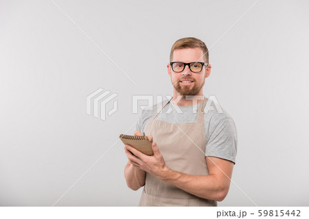 Happy young bearded waiter writing down order of client in notepad Happy young bearded waiter writing down order of client in notepad 59815442
