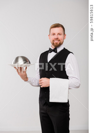Happy young waiter in black waistcoat and bowtie holding white towel and cloche Happy young waiter in black waistcoat and bowtie holding white towel and cloche 59815613
