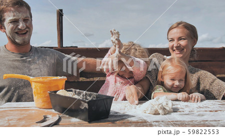 The young family knead the dough for bread and throw flour at each other. The young family knead the dough for bread and throw flour at each other. 59822553