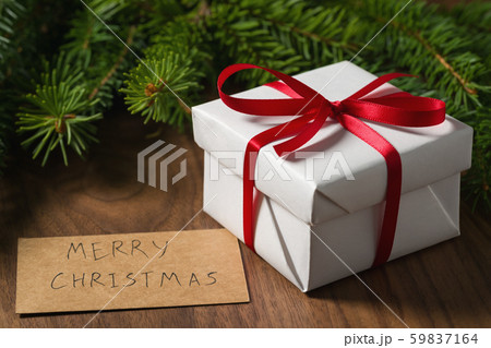 white gift box with red ribbon and paper card near spruce twig on walnut table 59837164