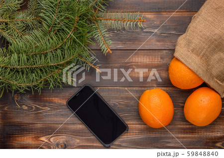 Oranges in a linen bag on a wooden background. Near fir branches and black smartphone. Christmas 59848840
