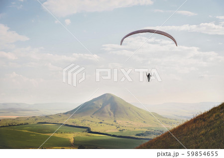 A white-orange paraglider flies over the mountainous terrain 59854655