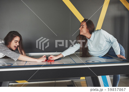 Two beautiful twin girls play air hockey in the game roomand have fun Two beautiful twin girls play air hockey in the game roomand have fun 59857867