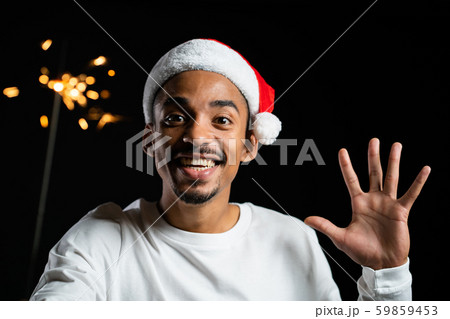 African american man in Santa hat celebrating with sparkler and bengal fire. African american man in Santa hat celebrating with sparkler and bengal fire. 59859453