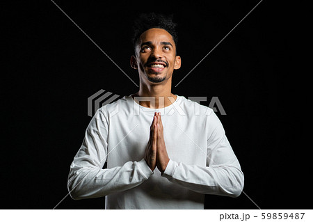 Handsome african american man in white t-shirt praying over black background. Handsome african american man in white t-shirt praying over black background. 59859487
