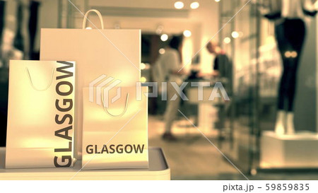 Paper shopping bags with Glasgow caption against blurred store entrance. Retail in the United 59859835