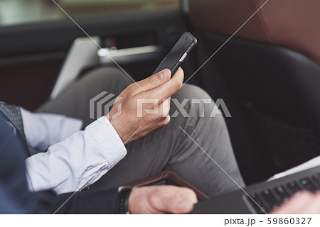 A businessman who sends a message to a smartphone and goes to the car's rear seat. A businessman who sends a message to a smartphone and goes to the car's rear seat. 59860327