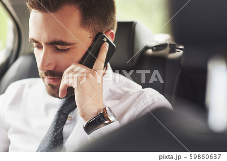 A businessman who sends a message to a smartphone and goes to the car's rear seat. 59860637