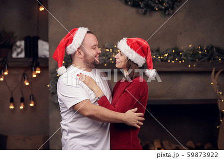 Side portrait of embracing happy men and women in Santa's cap in room Side portrait of embracing happy men and women in Santa's cap in room 59873922