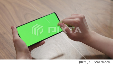 Young woman sitting at a table and using a smartphone with horizontal green screen Young woman sitting at a table and using a smartphone with horizontal green screen 59876220