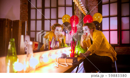 A sad man clown sitting in front of the mirror and smoking a cigarette A sad man clown sitting in front of the mirror and smoking a cigarette 59883380