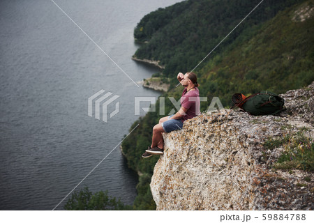 Traveller with backpack sitting on top of mountain enjoying view above the water surface. Traveling Traveller with backpack sitting on top of mountain enjoying view above the water surface. Traveling 59884788