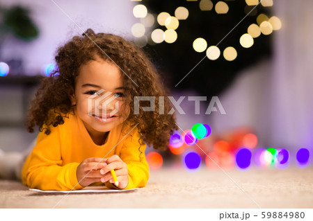 Adorable little afro girl lying on floor near Xmas tree Adorable little afro girl lying on floor near Xmas tree 59884980