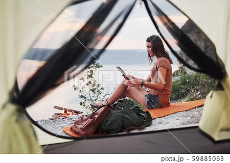 View from tent of woman traveller with backpack sitting on top of mountain enjoying view coast a 59885063
