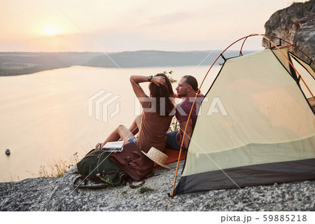 Photo of happy couple sitting in tent with a view of lake during hiking trip. Travel Lifestyle Photo of happy couple sitting in tent with a view of lake during hiking trip. Travel Lifestyle 59885218