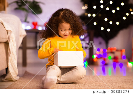 Stunned little african kid looking into Christmas gift box Stunned little african kid looking into Christmas gift box 59885273