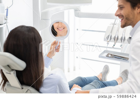 Sattisfied woman client of dental clinic smiling at mirror Sattisfied woman client of dental clinic smiling at mirror 59886424