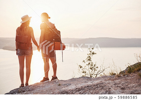 Two tourist male and woman with backpacks stand to the top of the crag and enjoying sunrise 59886585