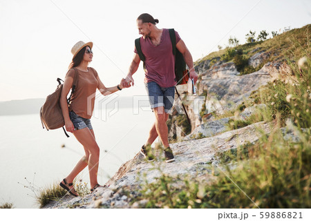 Two tourist male and woman with backpacks climb to the top of the mountain and enjoying sunrise Two tourist male and woman with backpacks climb to the top of the mountain and enjoying sunrise 59886821