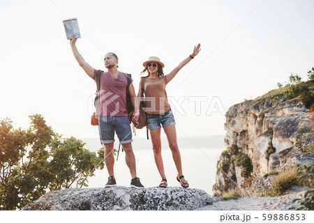 Two tourist male and woman with backpacks stand to the top of the crag and enjoying sunrise 59886853