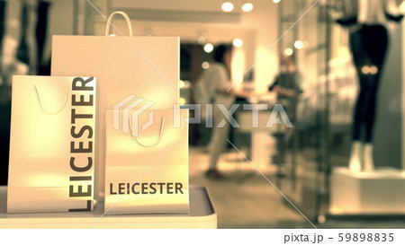 Paper shopping bags with Leicester caption against blurred store entrance. Retail in the United 59898835