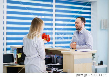 A beautiful young girl in a white coat is standing near the desk in the office and taking boquet of A beautiful young girl in a white coat is standing near the desk in the office and taking boquet of 59901182