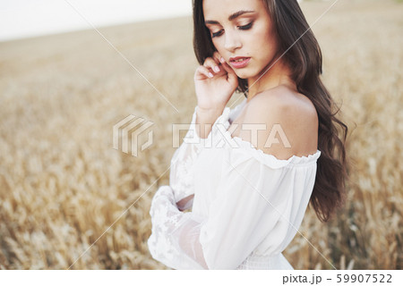Young sensitive girl in white dress posing in a field of golden wheat Young sensitive girl in white dress posing in a field of golden wheat 59907522