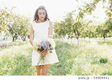 Beautiful young woman wearing elegant white dress and enjoying beautiful sunny afternoon in a summer 59908441