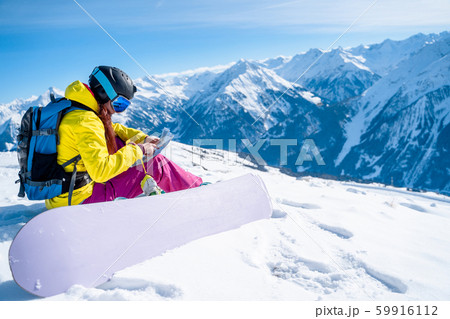 Image of snowboarder girl in helmet with map in her hands sitting on mountain slope 59916112