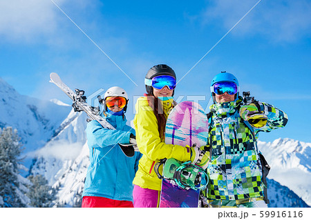 Sportsmen and woman with snowboard and skis standing on snow resort against background of mountain 59916116