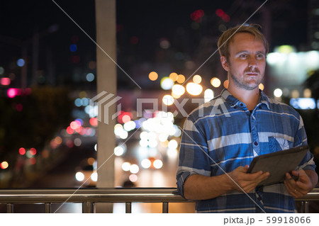 Handsome businessman thinking while using digital tablet at night Handsome businessman thinking while using digital tablet at night 59918066