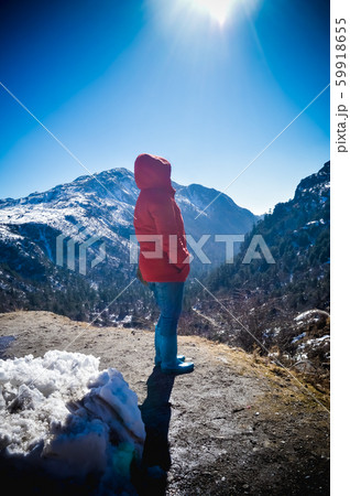 A woman in winter warm clothing standing on top of the rock of a snowcapped rocky mountain peak. 59918655