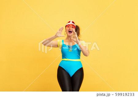 Young caucasian plus size female model's training on yellow background 59919233