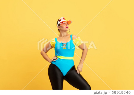Young caucasian plus size female model's training on yellow background Young caucasian plus size female model's training on yellow background 59919340