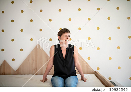 Front view of young woman sitting on bed in bedroom indoors at home. 59922546