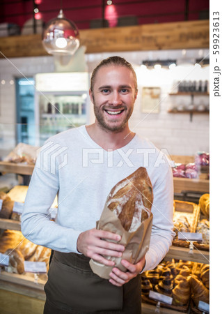 Smiling bearded man holding just baked bread standing in bakery Smiling bearded man holding just baked bread standing in bakery 59923613