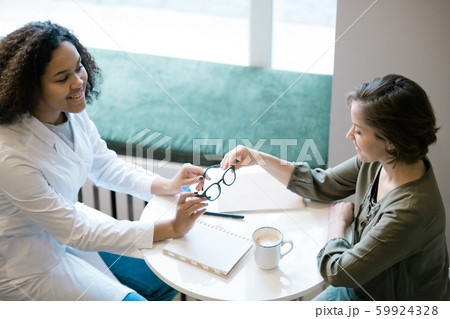 Young clinician in whitecoat consulting patient or client about new eyeglasses 59924328
