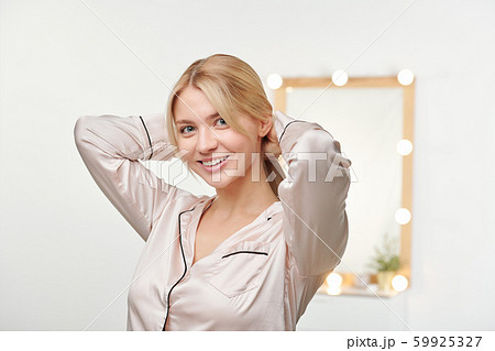 Healthy young female in silk pajamas keeping her hands on backhead Healthy young female in silk pajamas keeping her hands on backhead 59925327