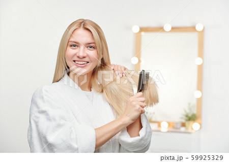 Happy and healthy young woman with toothy smile brushing her long blond hair Happy and healthy young woman with toothy smile brushing her long blond hair 59925329