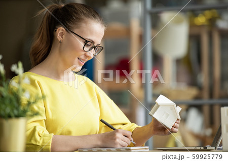 Successful young female architect with house model in hand looking through notes 59925779